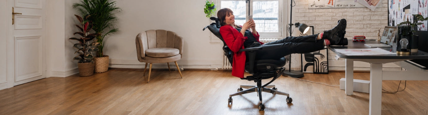 Femme installée dans une chaise de bureau ergonomique, les pieds posés sur un bureau assis-debout